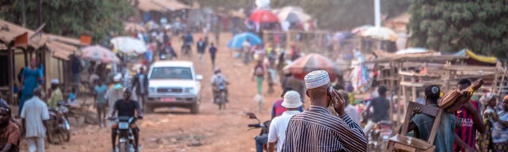 A busy, dusty street with cars, people, and motorcycles in rural Zambia.