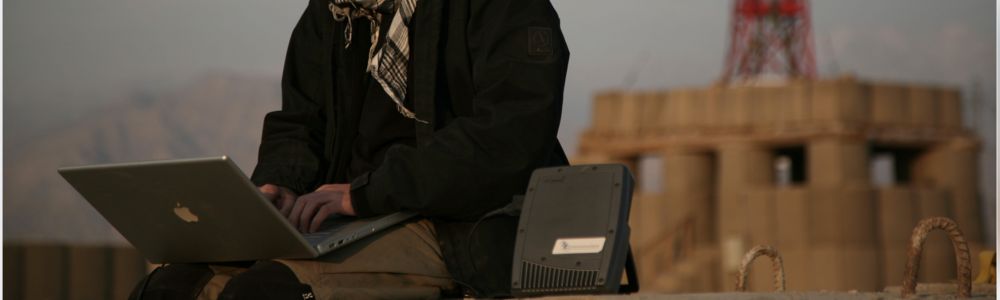 A man workin on his laptop outdoors in a remote setting and smoking a cigarette.