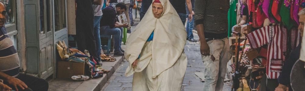 En kvinna som går på en gata bland folk och kommers i Tunisien