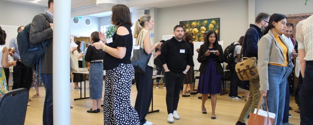 12 people sat at a rectangle of desks discussing a topic with whiteboards at the back. 