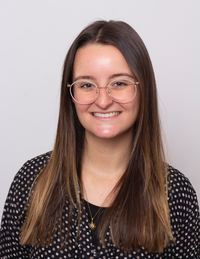 Young brunette woman in a black shirt against an off-white backdrop. 